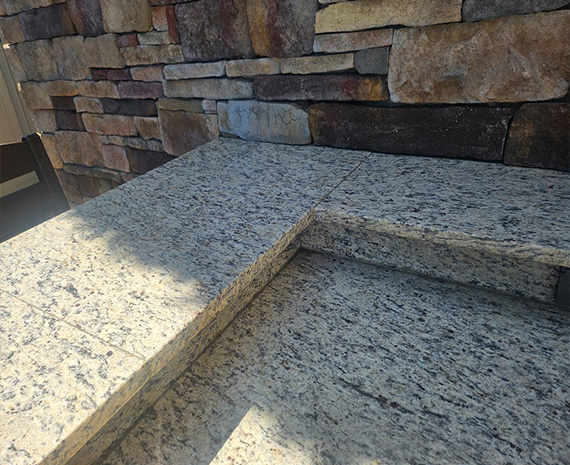 Outdoor granite steps beside a stone wall, with sunlight casting shadows on the treads.