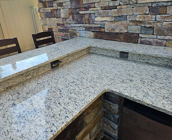 Outdoor granite countertop with speckled surface and an L-shaped bar edge against a stacked-stone wall.