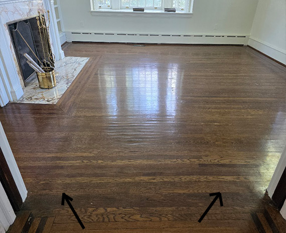 Empty room with dark polished hardwood floors; two black arrows mark the floor transition at the doorway threshold.