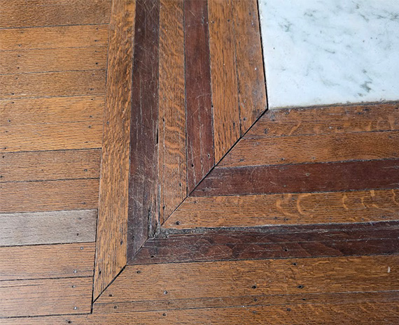 Close-up of a wooden parquet floor with a beveled frame border around a white marble tile corner.
