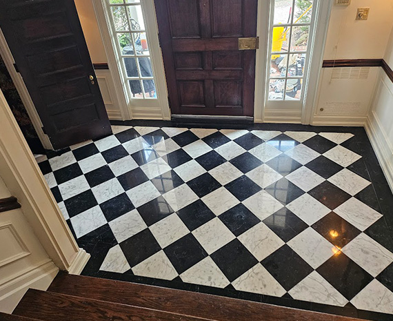 Entryway with black-and-white checkerboard tile floor, dark wooden front doors with glass sidelights.
