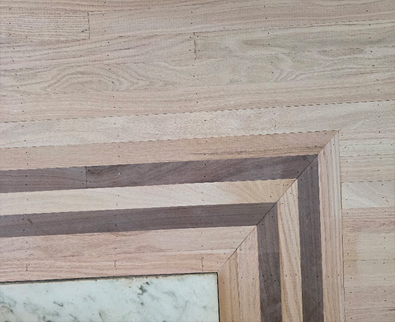 Close-up of a multi-layer wooden picture frame corner, showing alternating light and dark wood tones surrounding a marble inner panel.