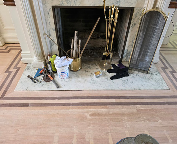 Tools and a bucket sit on a marble fireplace hearth during renovation, with a screen propped nearby and a pair of socks on the floor beside them.