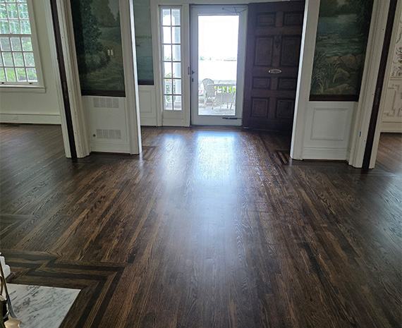 Wide entry hall with dark hardwood floors, white paneled walls, and a glass door that opens to an outdoor deck.