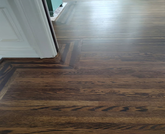 Dark brown hardwood floor with a decorative corner transition near a doorway and white trim