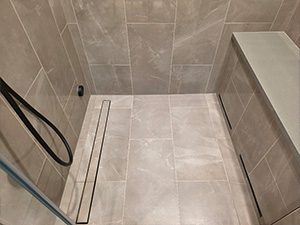 Walk-in shower with beige tile, a built-in bench on the right, a handheld showerhead, and a linear drain along the floor.