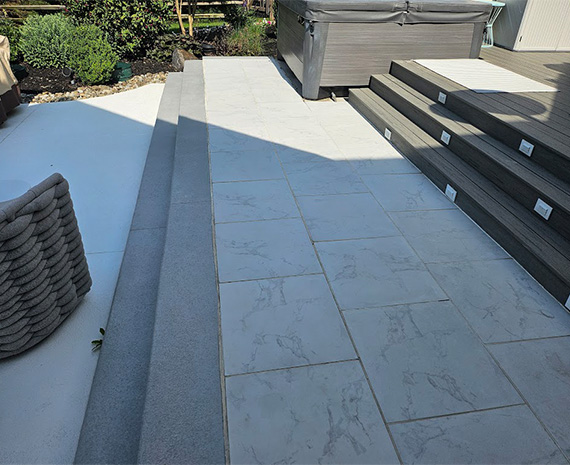 Outdoor patio with large gray marble-pattern tiles, wide steps, and a raised wooden deck on the right.