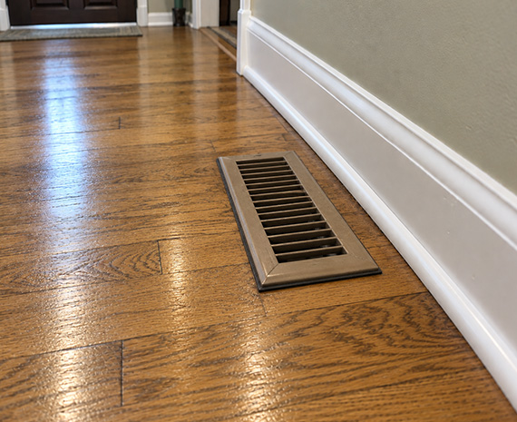 Old yellowed hardwood floor finish with raised metal HVAC vent before refinishing in Tabernacle, NJ.
